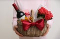 Woman holding wicker basket with gift, bouquet and wine on light grey background, closeup Royalty Free Stock Photo