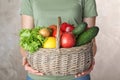Woman holding wicker basket with ripe fruits and vegetables on color background Royalty Free Stock Photo