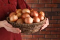 Woman holding wicker basket with ripe onions against red brick wall, closeup Royalty Free Stock Photo