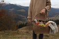 Woman holding wicker picnic basket with thermos, snacks and plaid in mountains on autumn day, closeup. Space for text Royalty Free Stock Photo