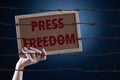 Woman holding wood board with PRESS FREEDOM text and rusty sharp bare wire on dark background, conceptual image. World press