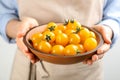 Woman holding wooden bowl of yellow tomatoes on light background, closeup Royalty Free Stock Photo