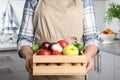 Woman holding wooden crate filled with fresh vegetables and fruits in kitchen Royalty Free Stock Photo