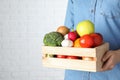 Woman holding wooden crate with fruits and vegetables at white brick wall, closeup Royalty Free Stock Photo