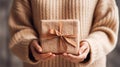 Woman Holding a Wrapped Gift in Cozy Setting. A person in warm, knitted sweater holds wrapped gift with a golden ribbon