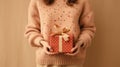 Woman Holding a Wrapped Gift in Cozy Setting. A person in warm, knitted sweater holds wrapped gift with a golden ribbon