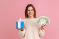 Woman holding wrapped present box and euro banknotes, looking at camera with positive expression. Royalty Free Stock Photo