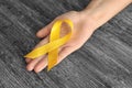 Woman holding yellow ribbon on wooden background. Cancer awareness concept Royalty Free Stock Photo