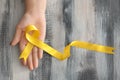 Woman holding yellow ribbon on wooden background. Cancer awareness concept Royalty Free Stock Photo