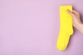 Woman holding yellow sock on light violet background, closeup. Space for text