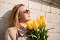 Woman holding yellow tulips, leaning against stone wall. Women& x27;s holiday concept, giving flowers. Royalty Free Stock Photo