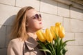 Woman holding yellow tulips, leaning against stone wall. Women& x27;s holiday concept, giving flowers. Royalty Free Stock Photo