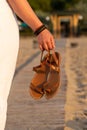 Woman holds brown leather sandals in her hand and looks at the beach hotel Royalty Free Stock Photo