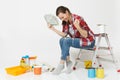 Woman holds bundle of dollars, cash money doing winner gesture, sitting on ladder with instruments for renovation Royalty Free Stock Photo