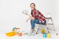 Woman holds bundle of dollars, cash money, sits on ladder with instruments for renovation apartment isolated on white Royalty Free Stock Photo