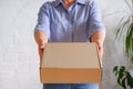 A woman holds a cardboard box on her outstretched hands against a background of a white brick wall