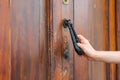 Woman holds hand knocker on old wooden door. Hand opens doors. Wooden carved door with rusted hand knocker. Royalty Free Stock Photo