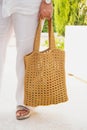 Woman holds a handmade beige knitted bag in her hand near her legs outdoors. Sustainable shopping. Wasteless lifestyle Royalty Free Stock Photo