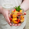 Woman holds in hands glass jar with fresh sliced fruits.