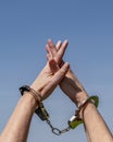 A woman holds her arms up to the sky with her hands bound by iron handcuffs