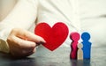 A woman holds in her hands a red heart near a miniature family. Concept of life and health insurance. Insurance agent services.