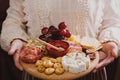 A woman holds in her hands a round wooden cutting board with Wine appetizers - slicing cheese, sausage and fruit Royalty Free Stock Photo
