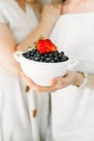 A woman holds in her hands a white bowl with ripe blueberries, on top of which lies a strawberry with the side bitten off Royalty Free Stock Photo