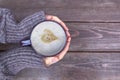 Woman holds hot cup of coffee latte, cappuccino with milk cream and heart valentine, love, warming her hands on wooden brown ba