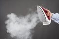 Woman holds an iron with steam on gray background