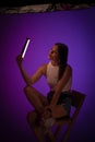 Woman holds LED lamp looking on it against of purple background. Presentation of Nanlite Studio Lighting. Backstage