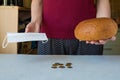 A woman holds a medical mask that protects against infection and covid-19 and a loaf of bread. The last money is on the table. Royalty Free Stock Photo