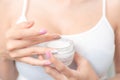 A woman holds a moisturizer in her hand and her skin and wrinkle from impurities