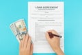 A woman holds money in her hand, reads and signs a loan agreement on the blue background Royalty Free Stock Photo