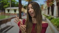 Woman holds open red ring box with both hands and inspects engagement ring beside a park bench; romance celebration commitment Royalty Free Stock Photo