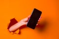 A woman holds a phone through ragged orange paper background, close-up. Royalty Free Stock Photo