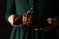 Woman holds plate tasty pancakes against dark brown background, close up