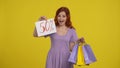 A woman holds shopping bags and shows the inscription fifty percent. Satisfied shopaholic woman in studio on yellow