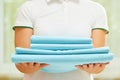A woman holds a stack of clean folded blue bedding. Blurred background. Close-up
