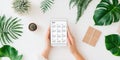 woman holds tablet displaying 2025 calendar surrounded by plants