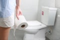 Woman holds toilet paper roll in front of toilet bowl.