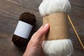 Woman holds white skein of hand`spun yarn with blank Kraft paper wrap label for mockup on rustic wooden table with needles.
