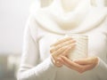 Woman holds a winter cup close up. Woman hands with elegant french manicure nails design holding a cozy knitted mug.