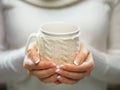 Woman holds a winter cup close up. Woman hands with elegant french manicure nails design holding a cozy knitted mug.