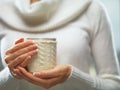 Woman holds a winter cup close up. Woman hands with elegant french manicure nails design holding a cozy knitted mug. Royalty Free Stock Photo