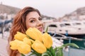 Woman holds yellow tulips in harbor with boats docked in the background., overcast day, yellow sweater, mountains Royalty Free Stock Photo