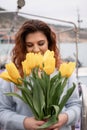 Woman holds yellow tulips in harbor with boats docked in the background., overcast day, yellow sweater, mountains Royalty Free Stock Photo