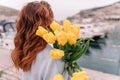 Woman holds yellow tulips in harbor with boats docked in the background., overcast day, yellow sweater, mountains Royalty Free Stock Photo