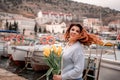 Woman holds yellow tulips in harbor with boats docked in the background., overcast day, yellow sweater, mountains Royalty Free Stock Photo