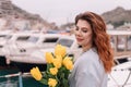 Woman holds yellow tulips in harbor with boats docked in the background., overcast day, yellow sweater, mountains Royalty Free Stock Photo