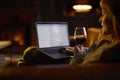 Woman At Home In Lounge Lying On Sofa With Cosy Fire Checking Emails On Laptop Holding Glass Of Wine Royalty Free Stock Photo